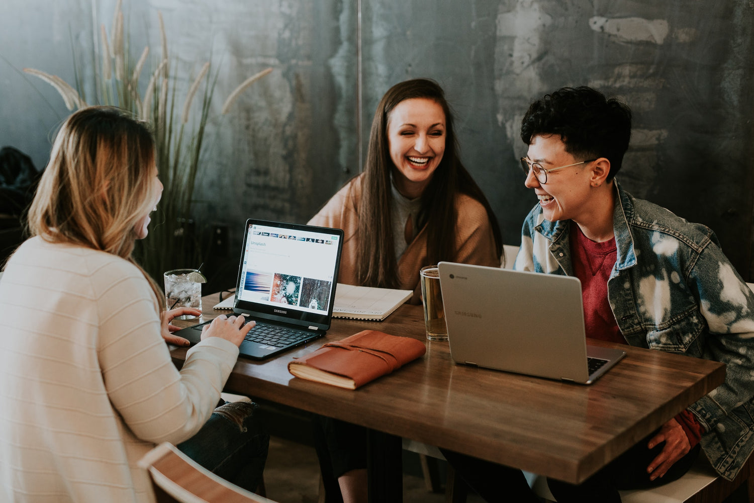 Three Young People Laughing at a Table with Laptops